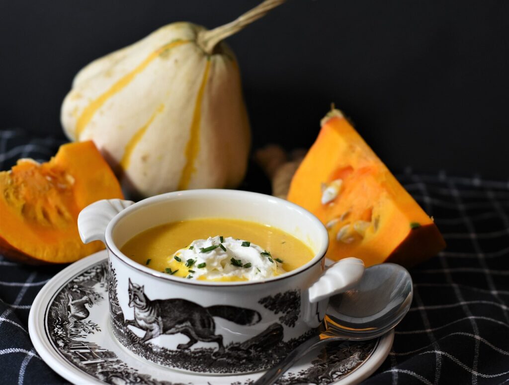 Creamy butternut soup served in a vintage bowl with fresh herbs, surrounded by sliced pumpkin on a dark background.