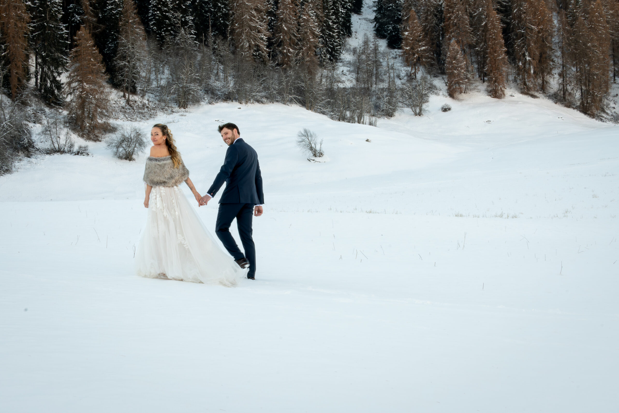 Bridgette and her husband walking hand in hand through the snowy Swiss Alps on their wedding day, surrounded by winter trees and mountain silence.